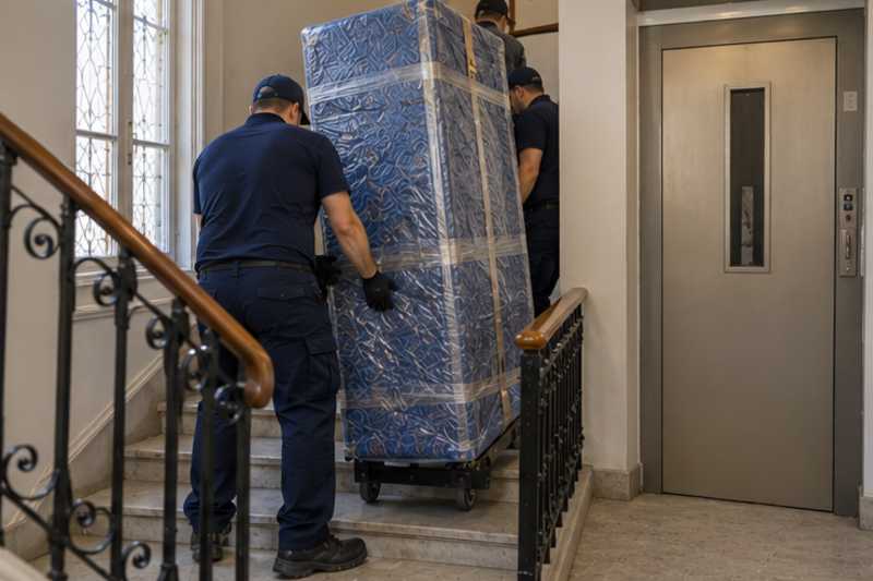 Un grand matelas debout sous couvertures capitonnées et film étirable, dans une cage d'escalier d'immeuble, déménagement de Paris vers l'Andorre