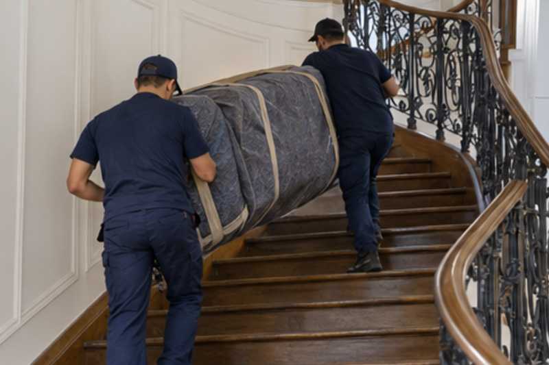 Un canapé convertible sous couverture de déménagement, dans un escalier tournant en bois d'immeuble ancien, déménagement de Paris vers l'Azerbaïdjan