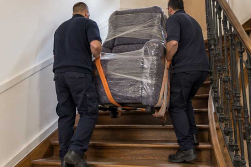 Un fauteuil releveur sous feutrine et film étirable, dans un escalier tournant en bois d'immeuble ancien, déménagement de Paris vers la Bosnie-Herzégovine