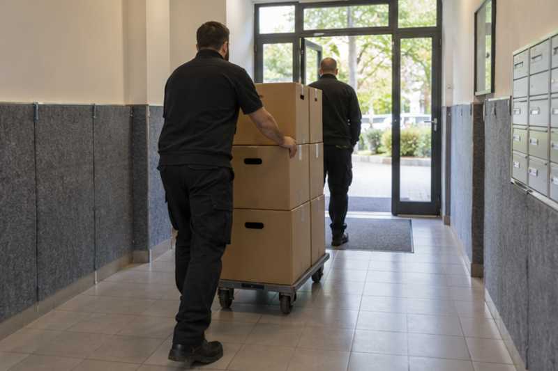 Une pile de cartons de déménagement fermés, dans le hall d'une résidence aux murs protégés par des panneaux de déménagement, déménagement de Paris vers le Cambodge