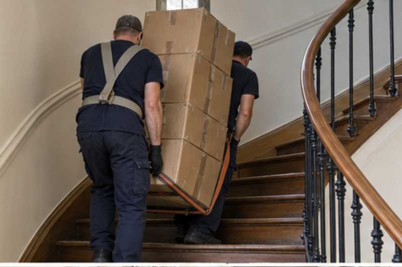 Une pile de cartons de déménagement fermés, dans un escalier tournant en bois d'immeuble ancien, déménagement de Paris vers le Honduras