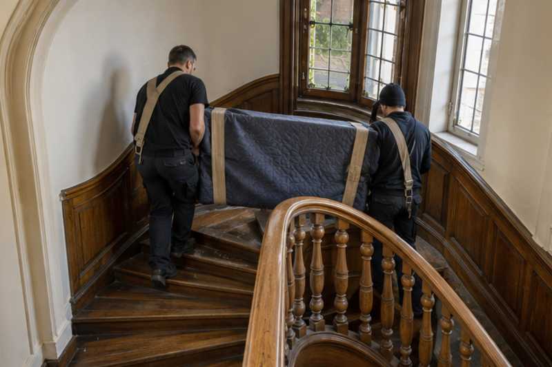 Un buffet bas sous couverture de déménagement, dans un escalier tournant en bois d'immeuble ancien, déménagement de Paris vers le Paraguay